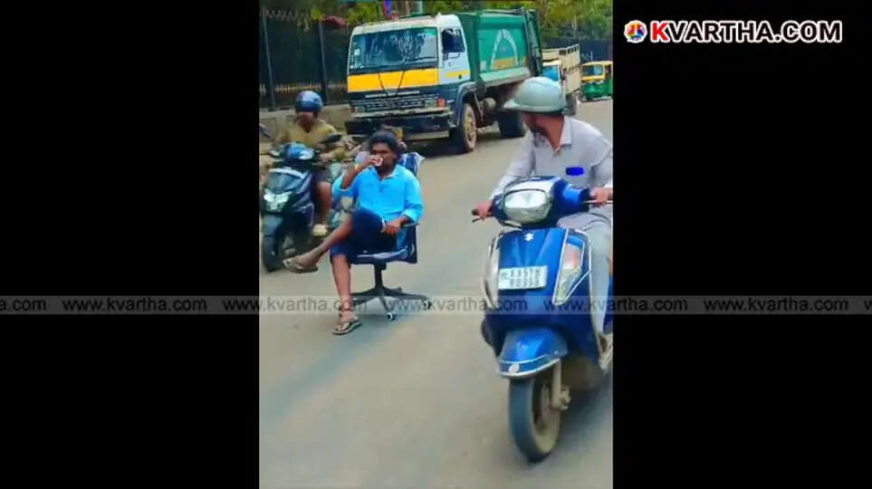 A young man sitting and drinking tea on a chair in the middle of a road